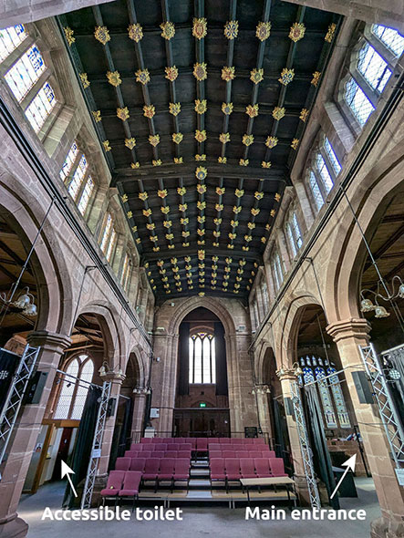 A photograph showing red, upholstered chairs on a small rake in the central nave of St Mary’s, with ceiling bosses above.  There are arrows and text showing where the accessible toilet and main entrance are on the image