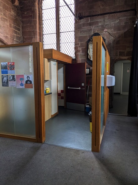 A photograph showing the entrance to the kitchen area.  This area is identified by the change in flooring from carpet to vinyl.  At the back of the area is the open door of the accessible toilet